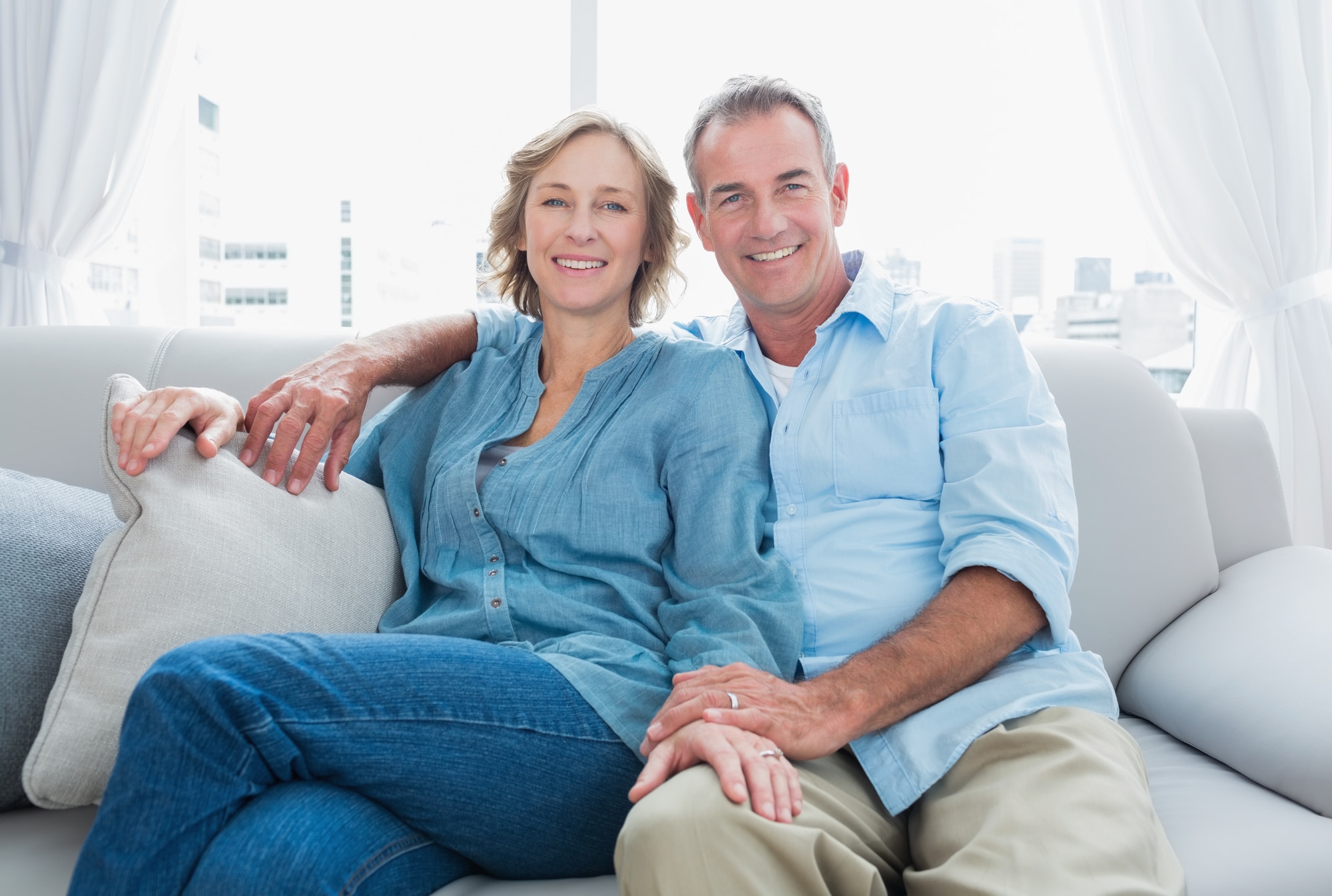 Guided Tissue Regeneration Columbus OH Middle aged couple relaxing on the couch smiling at camera at home in the living room